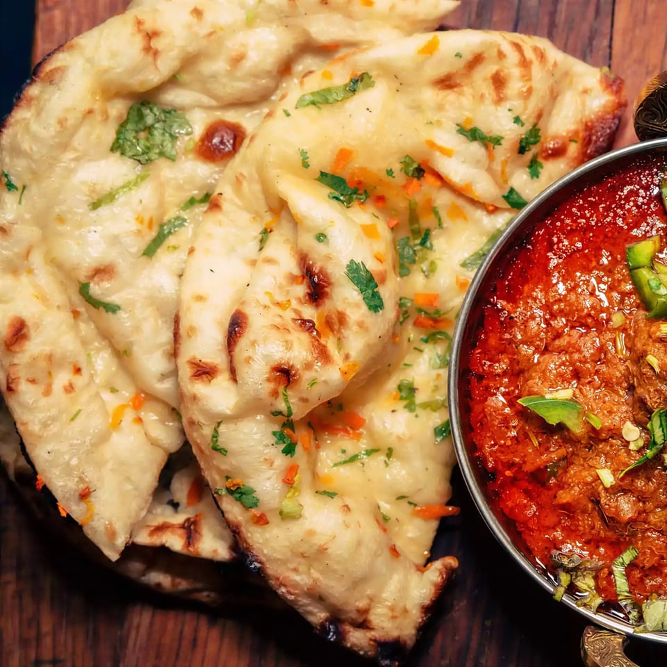Golden naan bread with herbs and spices next to a bowl of rich red curry.