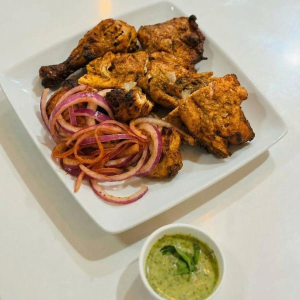Grilled chicken pieces and drumsticks with red onion slices, served with a green dipping sauce.