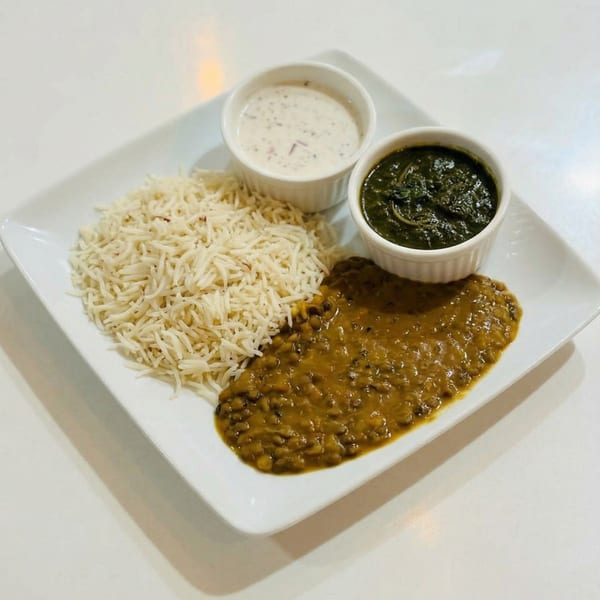 A white rectangular plate holds rice, dal, spinach, and raita, a complete Indian meal.
