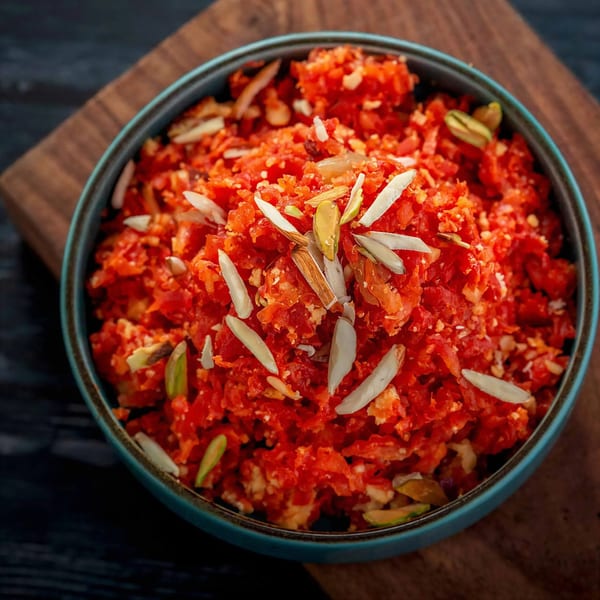 Close-up of a bowl of bright orange Gajar Halwa, garnished with slivered almonds and pistachios.