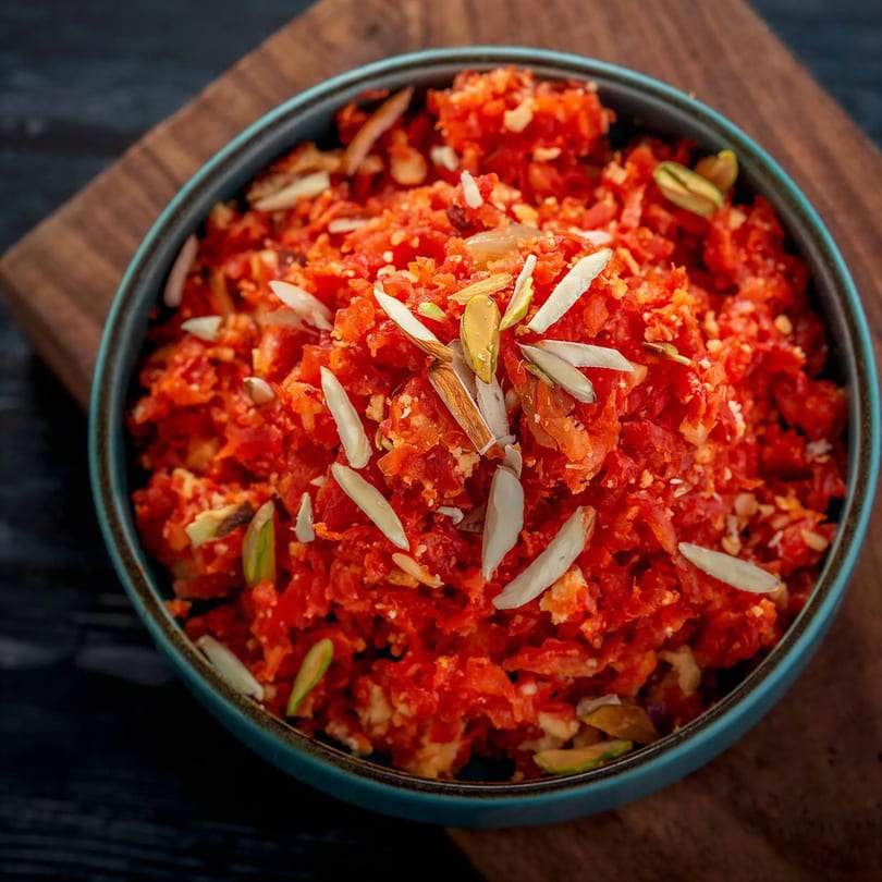Close-up of a bowl of bright orange Gajar Halwa, garnished with slivered almonds and pistachios.
